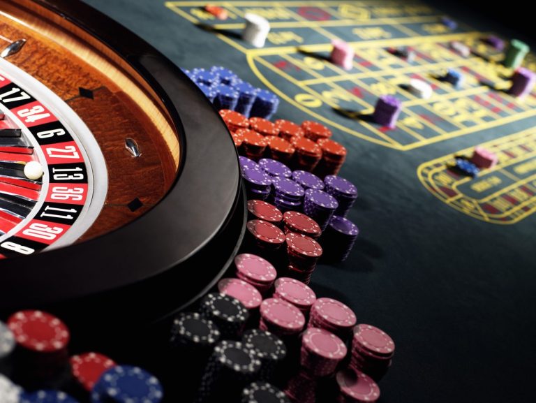 Close-up of a roulette wheel and colorful poker chips on a green casino table with betting areas.