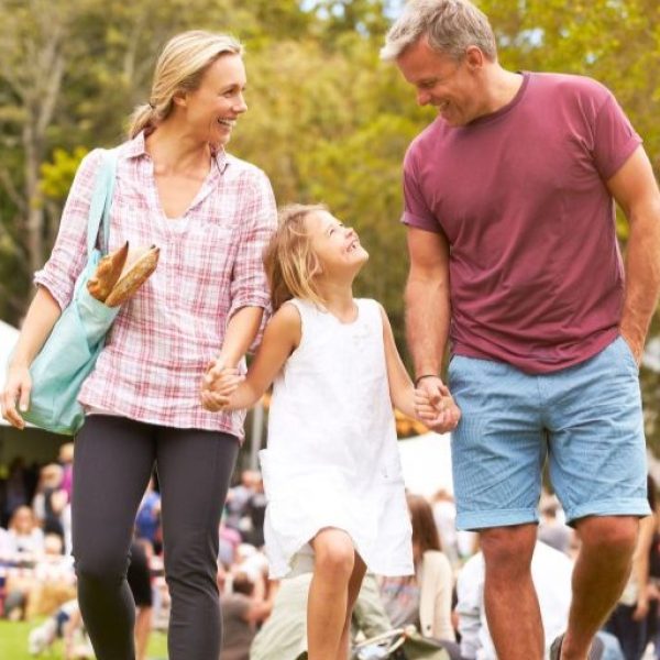 Smiling family with a young girl walking outdoors in a park, holding hands and carrying a bag with baguettes.